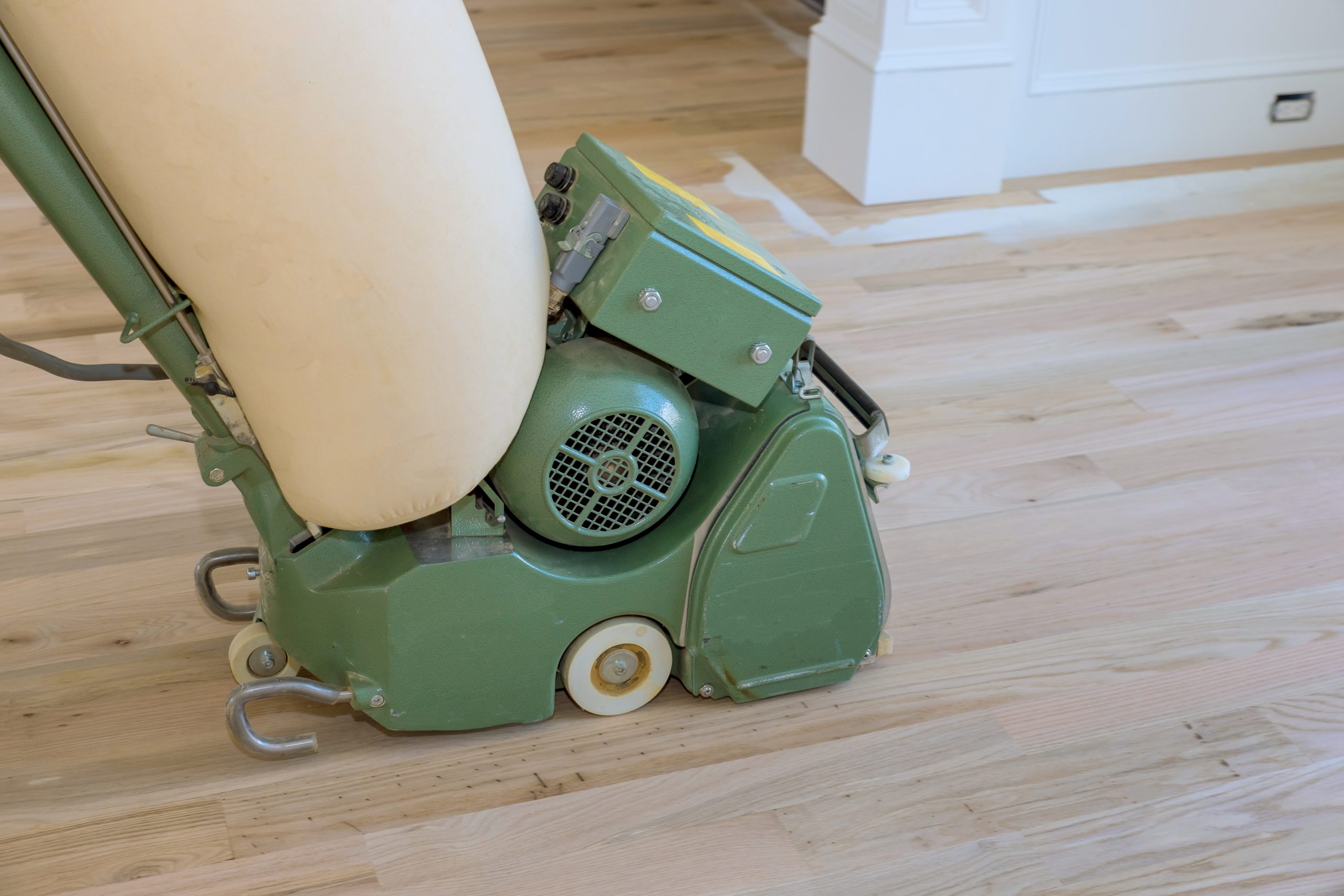 Wooden parquet floor being ground by carpenter using floor sander in newly constructed home