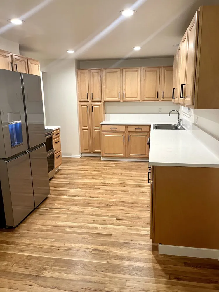 Kitchen remodel with natural maple cabinets, white quartz countertops, stainless steel appliances, and a newly installed hardwood floor.