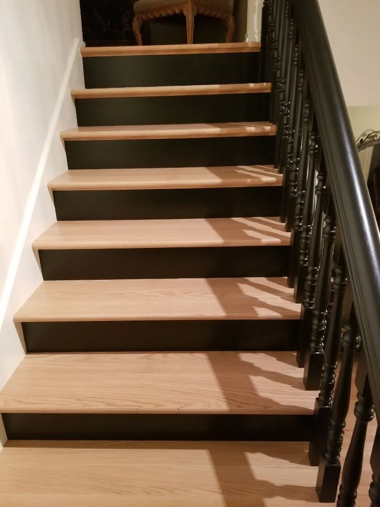 Modern staircase featuring natural wood treads contrasted with black painted risers and a traditional black spindle railing.