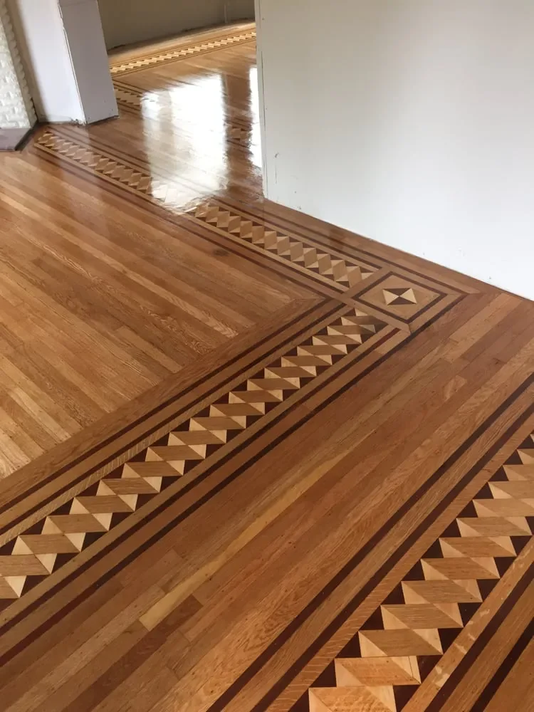 Custom hardwood floor inlay with a geometric parquet border design in light and dark wood tones during a home remodel.