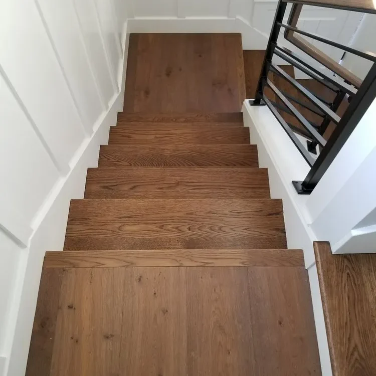 Top-down view of modern hardwood stairs with wide planks, white shiplap walls, and a black and wood railing
